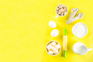 Baking ingredients and tools on trendy bright yellow background - flour, eggs, sugar, milk, butter, layout, flatlay top view copy space banner