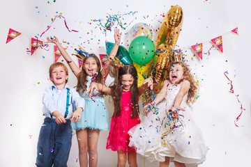 Group of beautiful kids throwing colorful confetti and looking happy on birthday party - obrazy, fototapety, plakaty