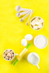 Baking ingredients and tools on trendy bright yellow background - flour, eggs, sugar, milk, butter, layout, flatlay top view copy space banner