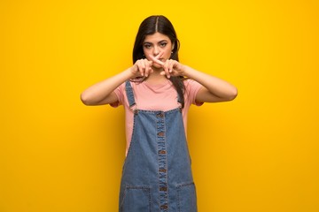 Teenager girl over yellow wall showing a sign of silence gesture