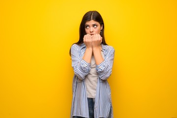 Teenager girl over yellow wall nervous and scared putting hands to mouth