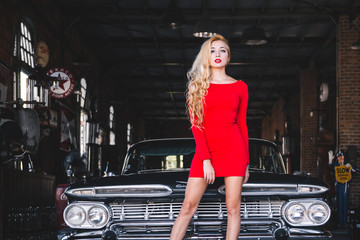 Sexy blond woman in red dress near retro car. Young sensual model posing for retro car show