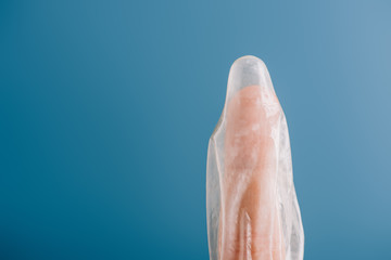 cropped view of finger with condom isolated on blue, contraception concept