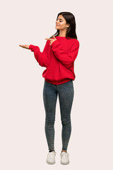A full-length shot of a Teenager girl with red sweater holding copyspace imaginary on the palm to...