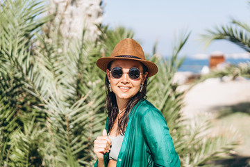 Cute pan asian girl in hat and sunglasses in green pareo walking on the seaside.