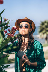 Cute pan asian girl in hat and sunglasses in green pareo walking on the seaside.