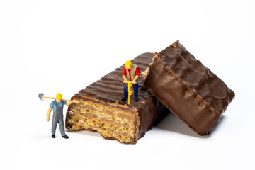 Miniature Workers Working On Chocolate Wafers, Isolated On White Background