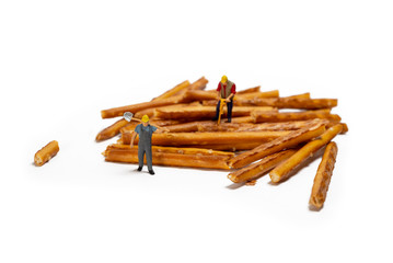 Miniature Workers Working On Stick Crackers, Isolated On White Background