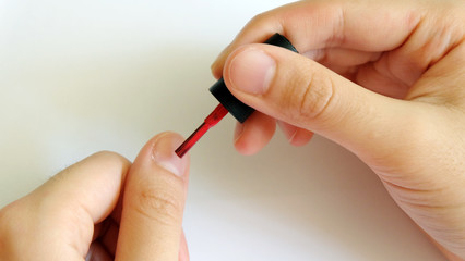 Hand applying red nail polish onto finger nail.