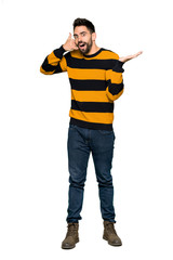 Full-length shot of Handsome man with striped sweater making phone gesture and doubting on isolated white background
