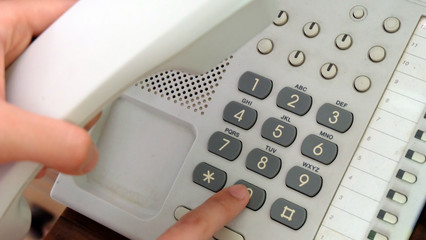 Finger dialing an office dial phone with many buttons when another hand is holding the receiver.