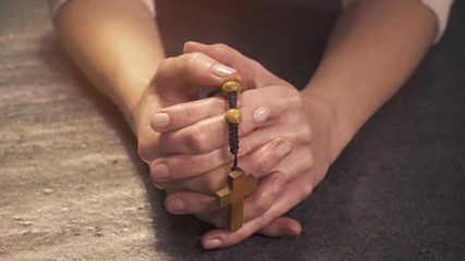 Woman praying with the rosary in her hands. Close-up of hands. Christian faith and traditions. Religion.