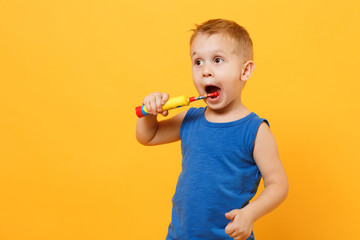 Kid boy 3-4 years old in blue shirt brush his teeth with toothbrush isolated on bright yellow...