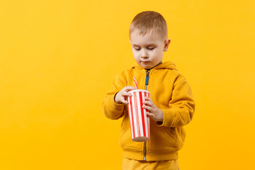 Little fun cheerful kid boy 3-4 years old wearing yellow clothes hold cup of soda isolated on orange wall background, children studio portrait. People, childhood lifestyle concept. Mock up copy space.
