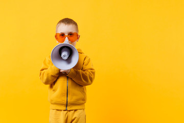 Little fun kid boy 3-4 years old in yellow clothes holding, speaking in electronic megaphone isolated on orange wall background, children studio portrait. People childhood concept. Mock up copy space.
