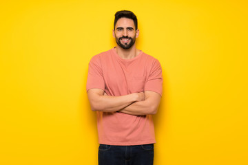 Handsome man over yellow wall keeping the arms crossed in frontal position