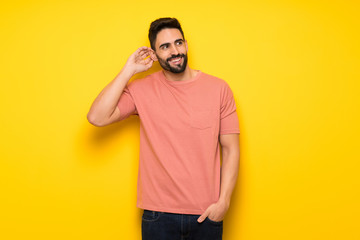 Handsome man over yellow wall thinking an idea while scratching head