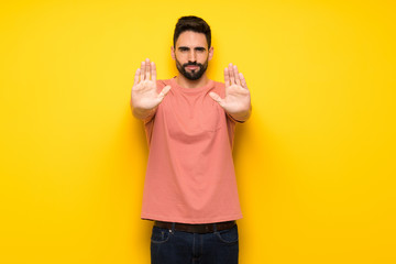 Handsome man over yellow wall making stop gesture for disappointed with an opinion