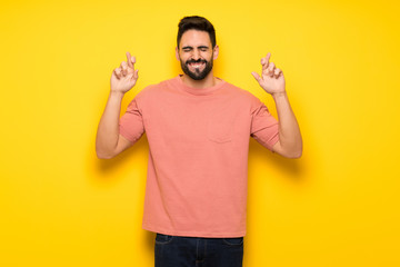 Handsome man over yellow wall with fingers crossing and wishing the best