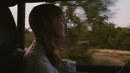 Happy little relaxed smiling girl tourist riding backwards inside safari car with hair blowing in the wind on excursion.