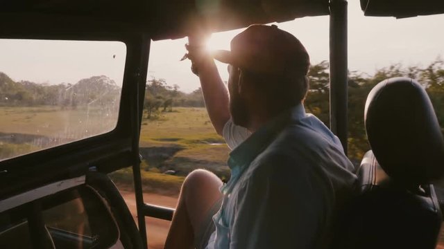 Young happy relaxing traveler man on epic sunset tropical forest excursion ride in safari car, sunlight shines through.