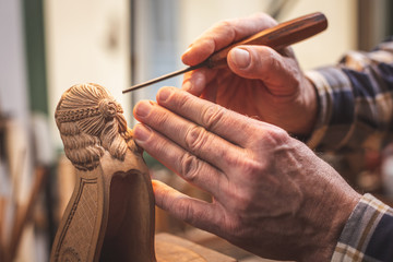 Hände eines Mannes beim Schnitzen einer Holzfigur