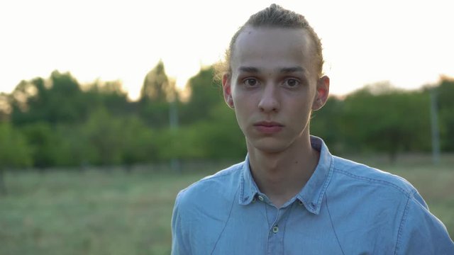 young handsome man looks at camera at sunset, outdoors, 4k