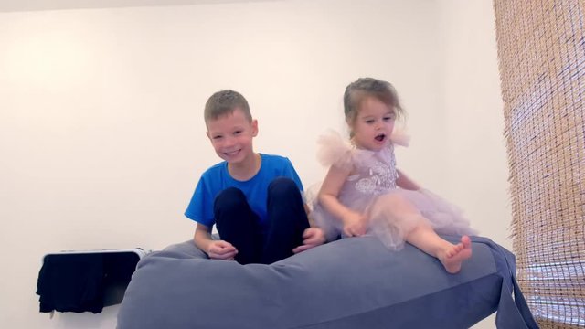 Brother and sister, girl in a beautiful dress sitting in a chair-bag in the nursery and playing.