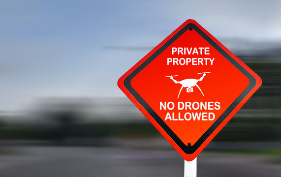 Private property sign, no drones allowed; A red aviation warning sign on a street, with speeding blurred background