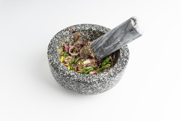 A mortar and pestle ( Lesung Batu) with mixed crushed chilies, shallots and anchovies on white background. Selective focus and crop fragment