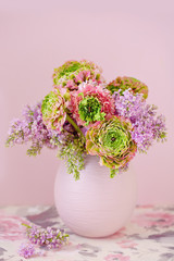 A beautiful bouquet of spring flowers with a lilac on a pink background.On the table with a beautiful tablecloth. Pastel colors.