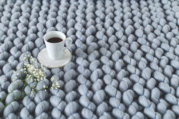 Obraz na płótnie Canvas Cup of coffee and gypsophila flowers on grey knitted woolen merino chunky blanket. Thick yarn.