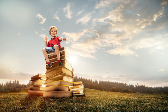 Little boy sitting on the tower made of big books. Childhood dreams, reading and education concept. Wondering world. abstract collage