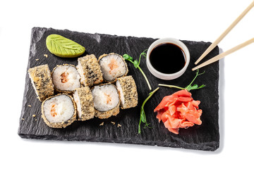 Concept of Japanese cuisine. Deep fried roll with salmon and mayonnaise in Panko bread crumbs. Near soy sauce, ginger and wasabi. Modern serving dishes in the restaurant on a black slate blackboard.
