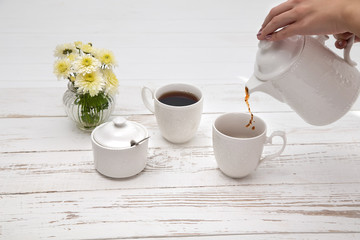 hands pours tea in cup of tea on wooden white table