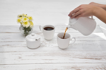hands pours tea in cup of tea on wooden white table