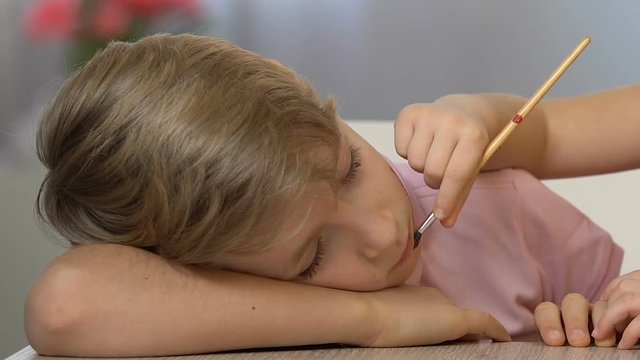 Small sister painting on face of sleeping boy, happy childhood, funny prank