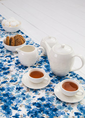 cups of tea with milk, cream and biscuits on wooden white table