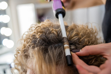 Fototapeta premium master doing curls, curl the hair with Curling iron, girl with blonde hair, close-up