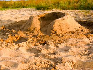 A simple sand wall made by children on the beach. Castle castle with a moat to play on the sand near the water.