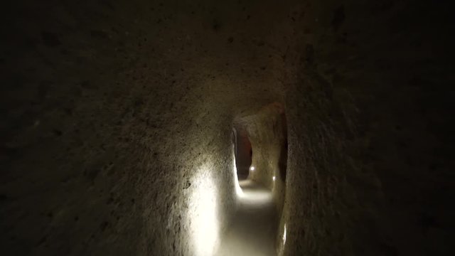 Dark Derinkuyu underground city caves in Cappadocia. Walking through ancient carved rock dwellings deep in the ground in Turkey. Long claustrophobic narrow passages.