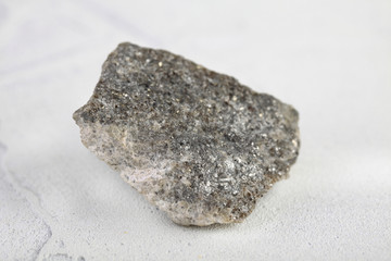 Fototapeta na wymiar Natural mineral rock specimen - raw Arsenopyrite stone on white cement background from Kachkarskoe, Ural, Russia