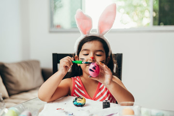 Fototapeta na wymiar Happy easter! A beautiful child girl painting Easter eggs. Happy family preparing for Easter. Cute little child girl wearing bunny ears on Easter day