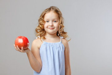 Portrait of an adorable little girl child holding in her hand a red apple. Gray background, studio