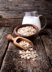 Oatmeal or oat flakes with milk on dark wooden table