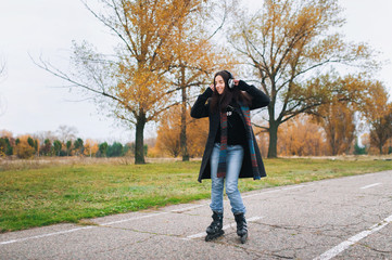 Young beautiful smiling girl in casual wear roller skating listens to music. Autumn walk in the fresh air.