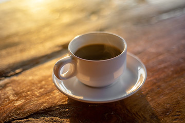 The hot coffee cup with smoke on the wooden table in the restaurant by retro style in the natural light. 