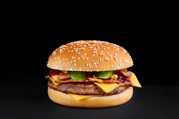 burger with beef cutlet, cheese, pickle, bacon and barbecue sauce isolated at black background