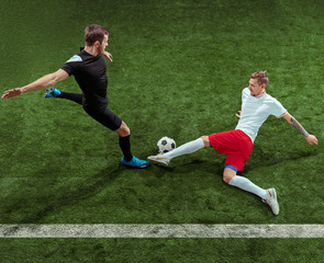 Football player tackling for ball over green grass background. Professional male soccer players in motion at stadium. Fit jumping men in action, jump, movement at game.