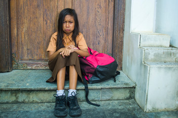 7 or 8 years child in school uniform sitting outdoors on the floor crying sad and depressed holding...
